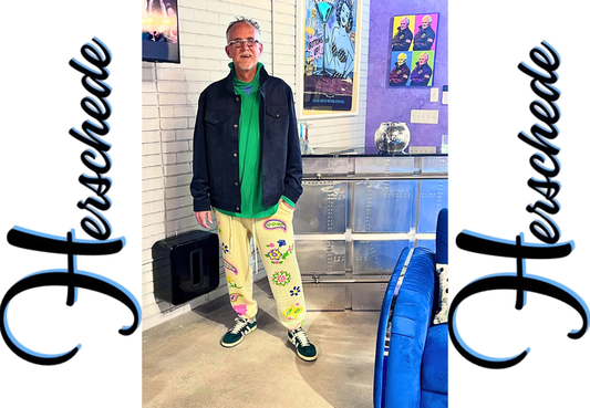 Picture of me in blue suede jacket, green hooide, cashmere cream joggers with colorful paisley and green suede shoes.  With Herschede logo on both sides positioned vertically