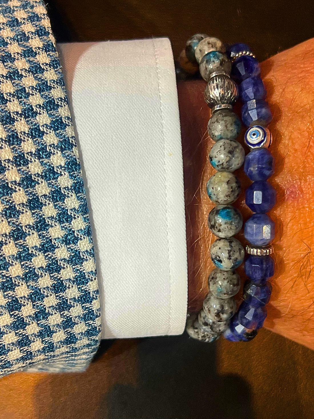 Picture of a man's wrist with a blue houndstooth coat sleeve, white dress shirt sleeve and two Tateossian beaded bracelets in blue